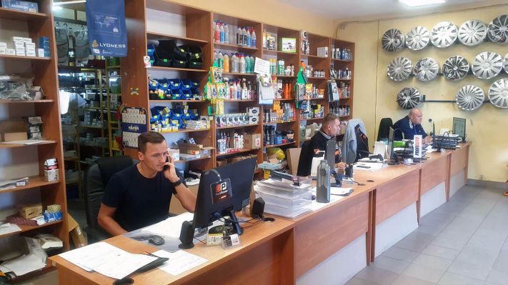 Sprzedawcy siedzący przy biurku w sklepie AUTKO, w tle regały z częściami samochodowymi