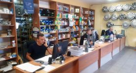 Sprzedawcy siedzący przy biurku w sklepie AUTKO, w tle regały z częściami samochodowymi